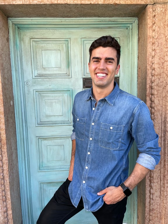 Gabe De Almeida smiling in a denim shirt, leaning against a green door